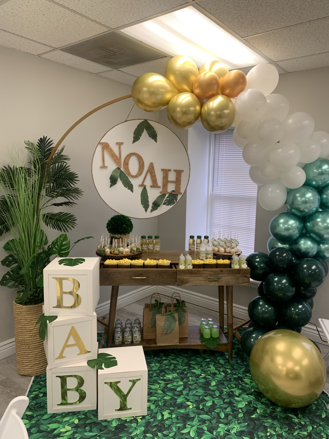 Gold and green baby shower display with balloon arch