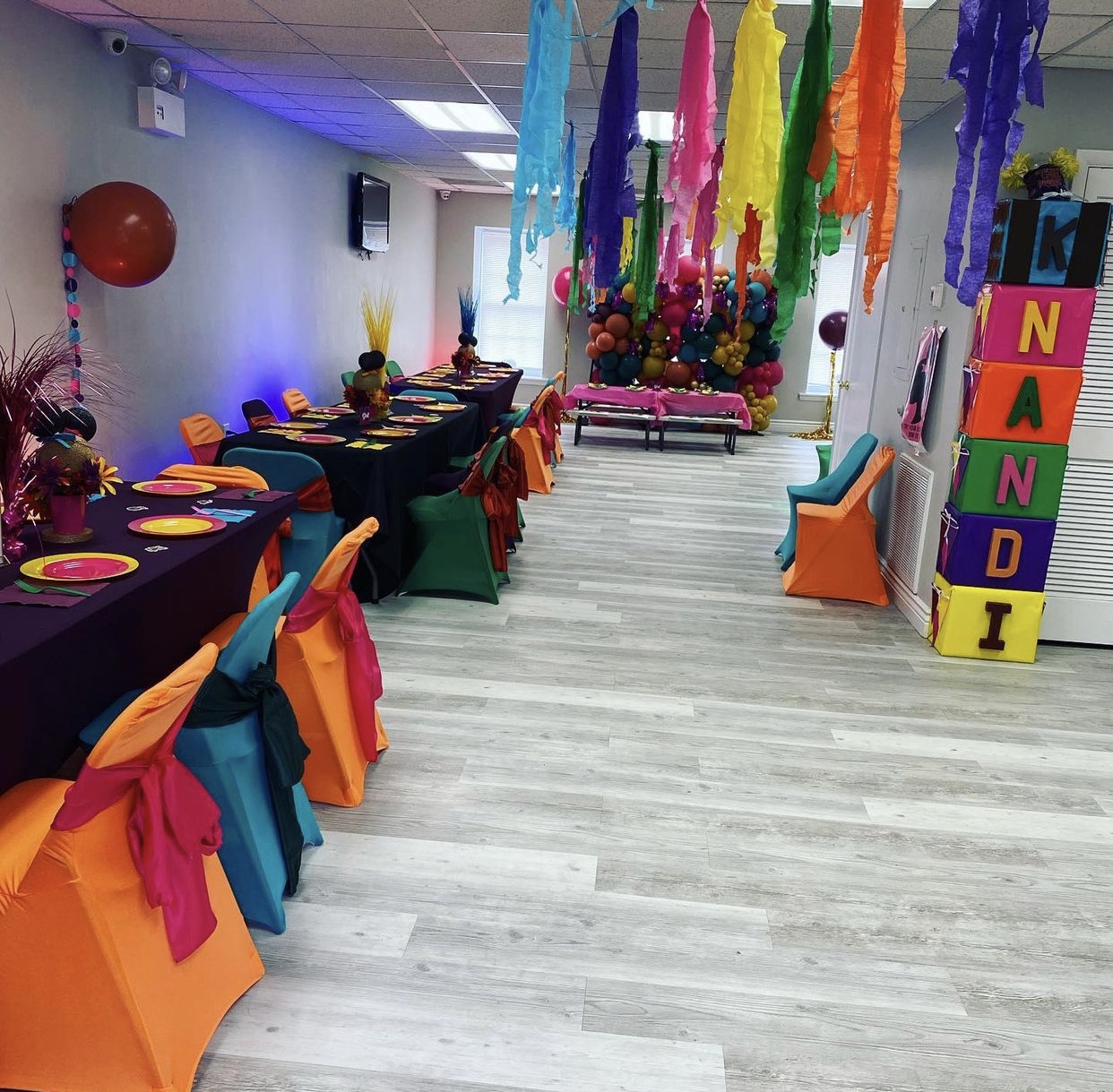 Rainbow party tables with colorful chair sashes and hanging decorations