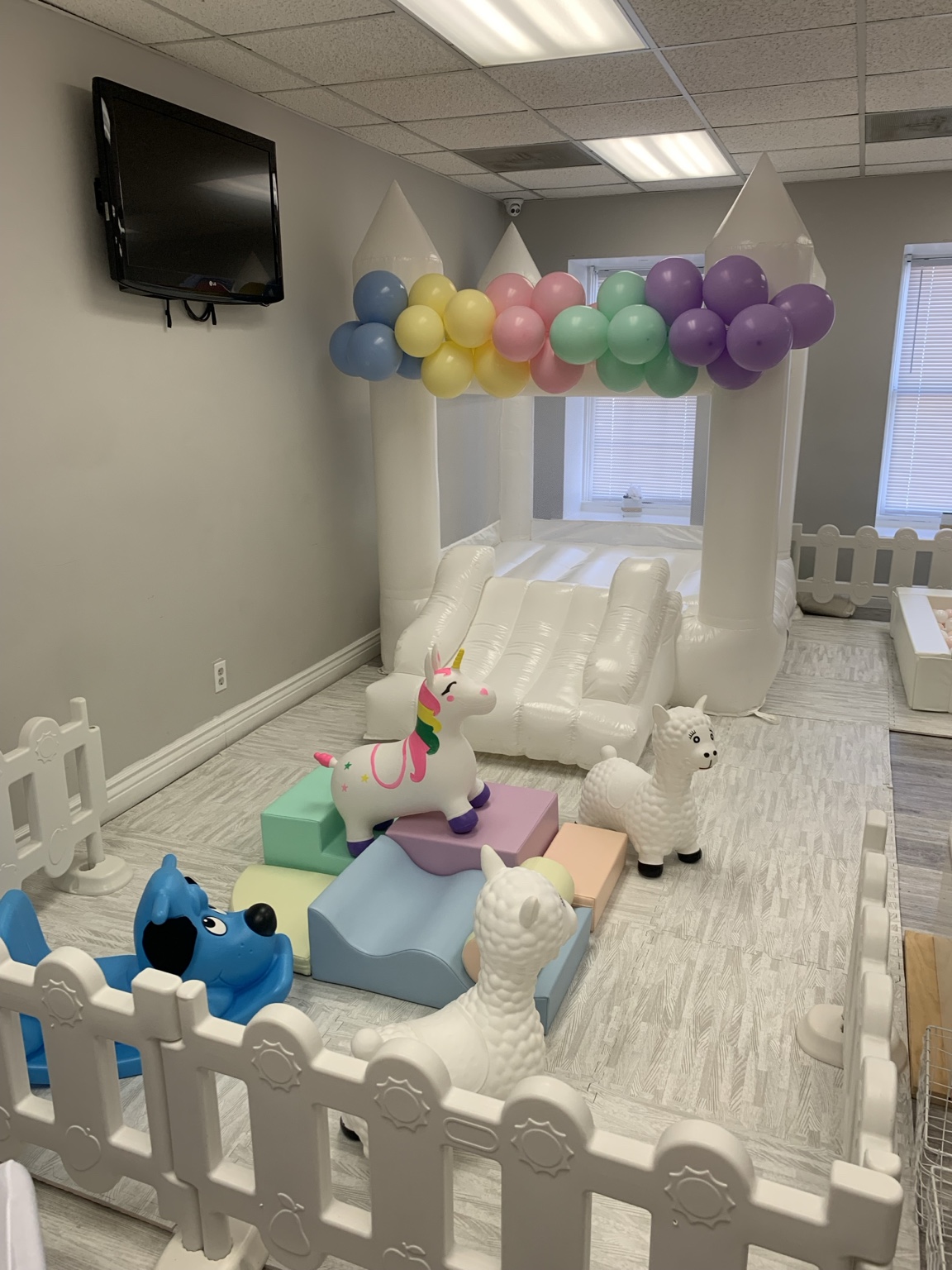 Pastel birthday play area with ride-on toys and balloon garland